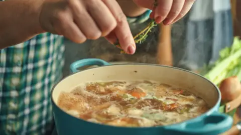 Getty Images Pot filled with food and person putting herbs in