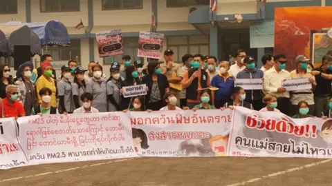 SOMJIT RUNGRASSAMEE /BBC THAI Local protesters this week wearing masks and calling for action with messages like 'Save Mae Sai'