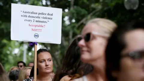 Getty Images A woman at a women's march holding a sign that says police respond to a domestic violence call every two minutes