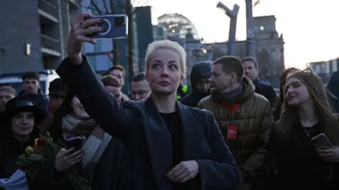 Sean Gallup/Getty Images Yulia Navalnaya, widow of late Russian opposition figure Alexei Navalny, does a selfie as the Reichstag stands behind after she voted in Russian elections on March 17, 2024 in Berlin, Germany