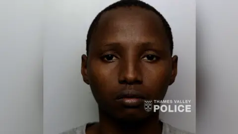 A mugshot of Edwine Kiplangat, who is expressionless and wearing a grey T-shirt.