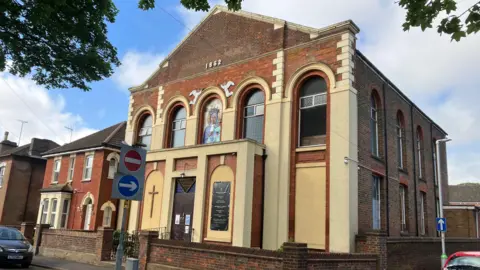 A picture of a Polish church in Dunstable that was built in the 19th century. It is two stories high and has a triangular roof. 
