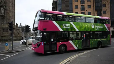 Getty Images A pink Translink double decker bus in the centre of Belfast. the bus has a large green advert on the side reason "Zero Emissions".