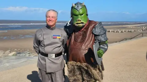 Neil Trickett A fan dressed in the uniform of the Empire in Star Wars along with one dressed as a Gamorrean Guard, a pig-like alien species from the Star Wars franchise.