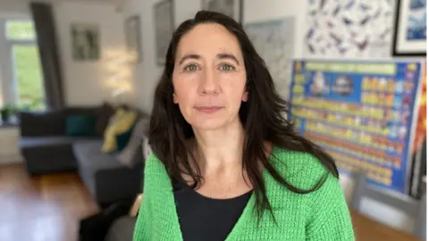 Naomi Campbell is looking at the camera and is wearing a green cardigan