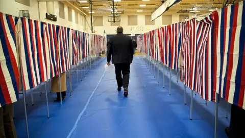 Getty Images A man walks past voting booths in New Hampshire in 2020
