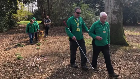 Blind visitors are guided on a walk through the arboretum