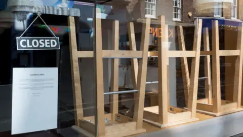 Getty Images Bar stools stacked on table behind a window displaying a closed sign