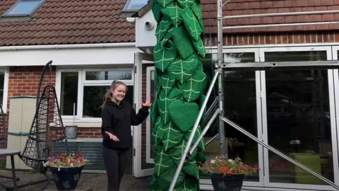 Ellen Wilkinson standing next to pantomime beanstalk in front of a house