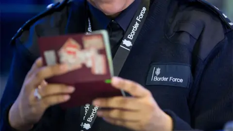 PA A UK Border Force officer checking a passport in Terminal 2 of London's Heathrow Airport