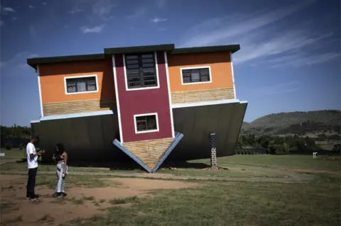 EPA Two people stand next to an upside-down house in Johannesburg, South Africa - Tuesday 15 February 2022