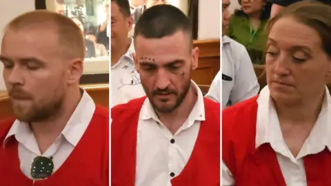 Three people wearing white shirts and red waistcoats. They are side-by-side and all looking down.