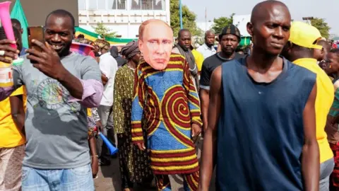 Getty Images A supporter of Malian Interim President wears a face mask of the President of Russia, Vladimir Putin, during a pro-Junta and pro-Russia rally in Bamako on May 13, 2022