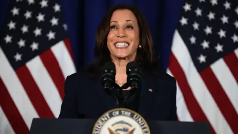 Getty Images Wearing a deep blue blazer and blouse, Kamala Harris smiles as she delivers a speech at the Louis Stokes Library on the Howard University campus in 2021