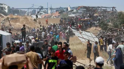 Reuters Crowds walk around damaged buildings to receive aid supplies from a Gaza Humanitarian Foundation distribution centre near an area of Gaza known as the Netzarim Corridor in central Gaza