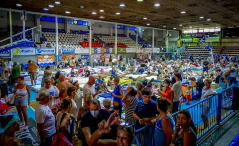 Argiris Mantikos/Eurokinissi via Reuters Tourists are sheltered in a stadium after being evacuated following a wildfire on the island of Rhodes