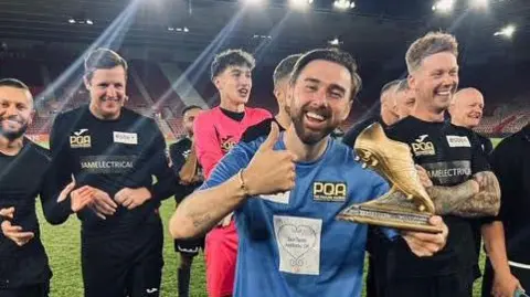 Sellebrity Soccer Charlie Quirke smiling with his thumbs up and holding a golden boot trophy