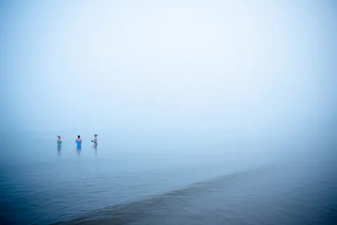 Anna Moffat Swimmers in the Mist - three distant people standing in the sea, surrounded by dense mist