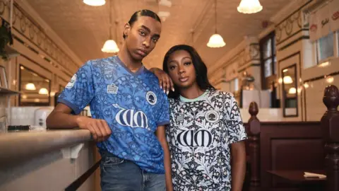 Jake Green Models pose in a Walthamstow pie and mash shop wearing home (left) and away shirts