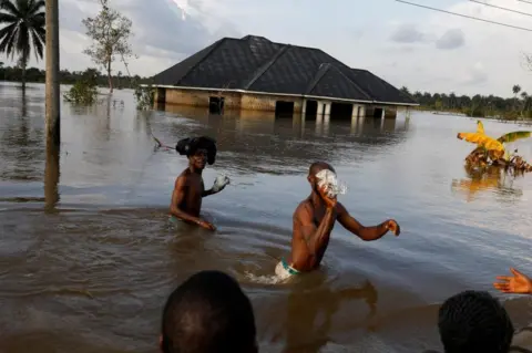 Reuters Topless men walking through flood waters. There is a submerged building behind them.
