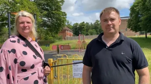 BBC A man and woman stood outside a children's playground