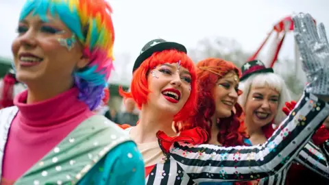 PA Media Performers in colourful costumes and wigs