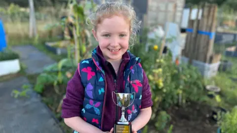 Kate Bradbrook/BBC Penny holding her trophy in a purple fleece in her allotment