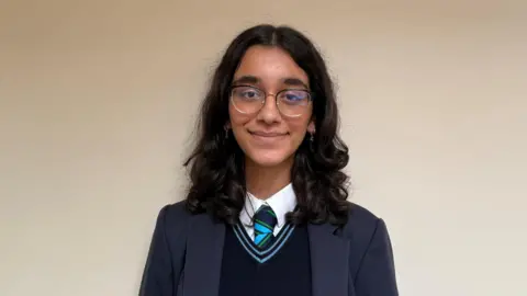 Siya. She has shoulder-length dark hair, wearing glasses and a navy school uniform.