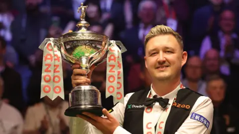 Kyren Wilson smiles while posting with the World Championship trophy
