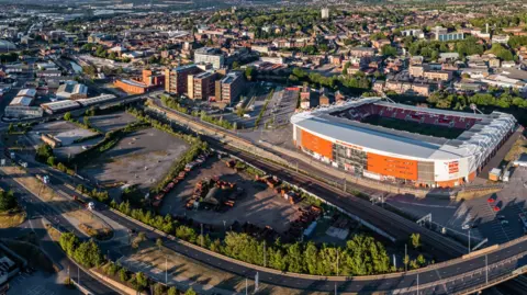 An aerial view of Rotherham town centre, with a large concentration of houses, flat blocks and a football stadium, circled by a road system.