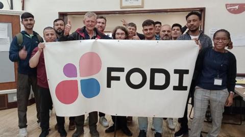 Steve Newman and a group of asylum seekers and refugees holding a FODI banner