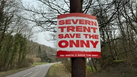 A large red and white sign on the side of a country road saying 'Severn Trent - Save the Onny'