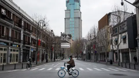 Getty Images A man by bicycles past an empty street on February 8, 2020 in Wuhan, Hubei province, China.