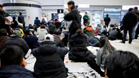 Reuters Kerabat penumpang pesawat yang jatuh setelah keluar dari landasan pacu, duduk di lantai bandara. 