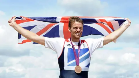 Getty Images Alan Campbell holding the union flag above his head, wearing a bonze medal