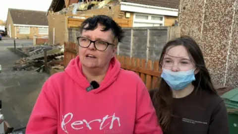 Marie Richards and her daughter Amy outside their home, which is surrounded by rubble