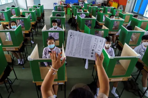ATHIT PERAWONGMETHA/Reuters Students wearing face masks in a classroom sit inside old ballot boxes repurposed into partitions