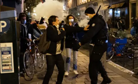 Getty Images Protester and policeman in street in Paris, with tear gas cloud, 23 Nov 20