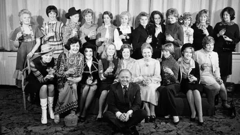 Getty Images/Mirrorpix Attenborough and Sim posing with 20 of the show's leading ladies