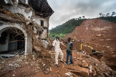 Olivia Acland Alfred Johnny talks to friend beside the broken house and mudslide