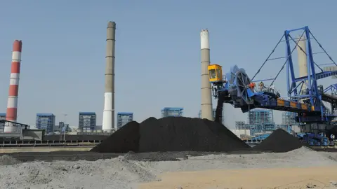Getty Images Workers use heavy machinery to sift through coal at the Adani Power company thermal power plant at Mundra
