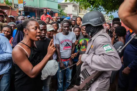 Getty Images A woman argues with a military guard as Haitians stand in line to receive a bag of food as part of the humanitarian aid provided by FAES (Fund for Economic and Social Assistance) on 16 August 2021 in Les Cayes, Haiti
