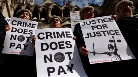 Getty Images Senior criminal lawyers hold placards outside the Royal Courts of Justice in London on July 4, 2022 as they go on strike in a dispute over pay.