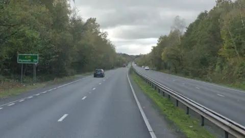 Google image shows the A38 heading toward Plymouth. Cars are travelling on both sides of the dual carriageway. A central reservation separates the two carriages. Trees line the dual carriageway. A sign which states A38 Plymouth 29 is on the left hand side. 