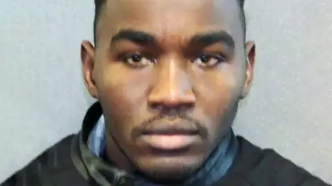 Police mugshot of Badreddin Abdalla Adam Bosh, with dark eyes, eyebrows and thin moustache and small beard on chin. Head and shoulders shot looking straight ahead at camera