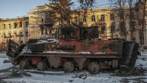 EPA A destroyed armoured troop-carrier stands in front of a destroyed building in Kharkiv, 11 March 2022.