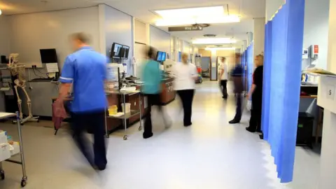 PA Media Staff in blue scrubs on a NHS hospital ward. They are slightly blurred because they are moving quickly