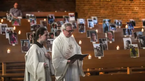 AFP Deacon Bernd Malecki and server Anna hold an Easter service in front of portraits of believers at the St. Barbara church in Oberhausen, western Germany.