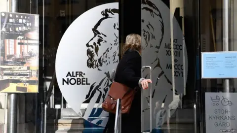 Getty Images A woman opens the door of the Alfred Nobel Museum in Stockholm, Sweden, that is located in the building where will be announced the winner of the 2017 Nobel Prize in Literature on October 5, 2017.