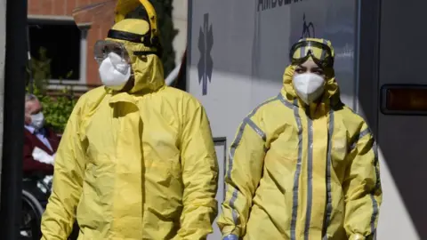 Getty Images Healthcare workers wearing protective suits stand at the entrance of the Severo Ochoa Hospital in Leganes, near Madrid, on April 03, 2020